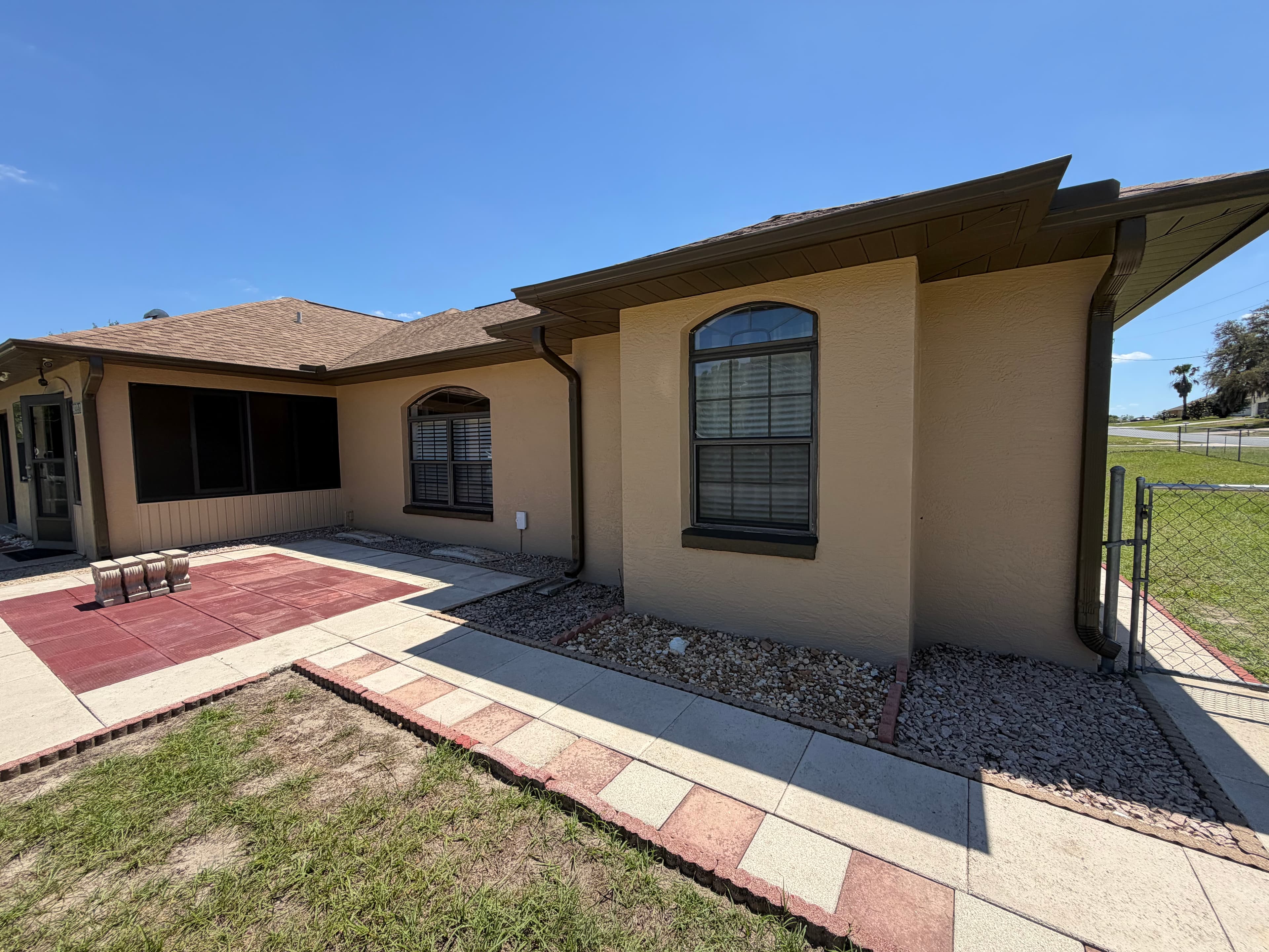 Tan house with brown roof, tiled patio, and walkway under a clear blue sky.
